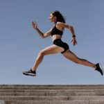 Energetic woman in active wear jumping on stairs outdoors, showcasing fitness and determination.